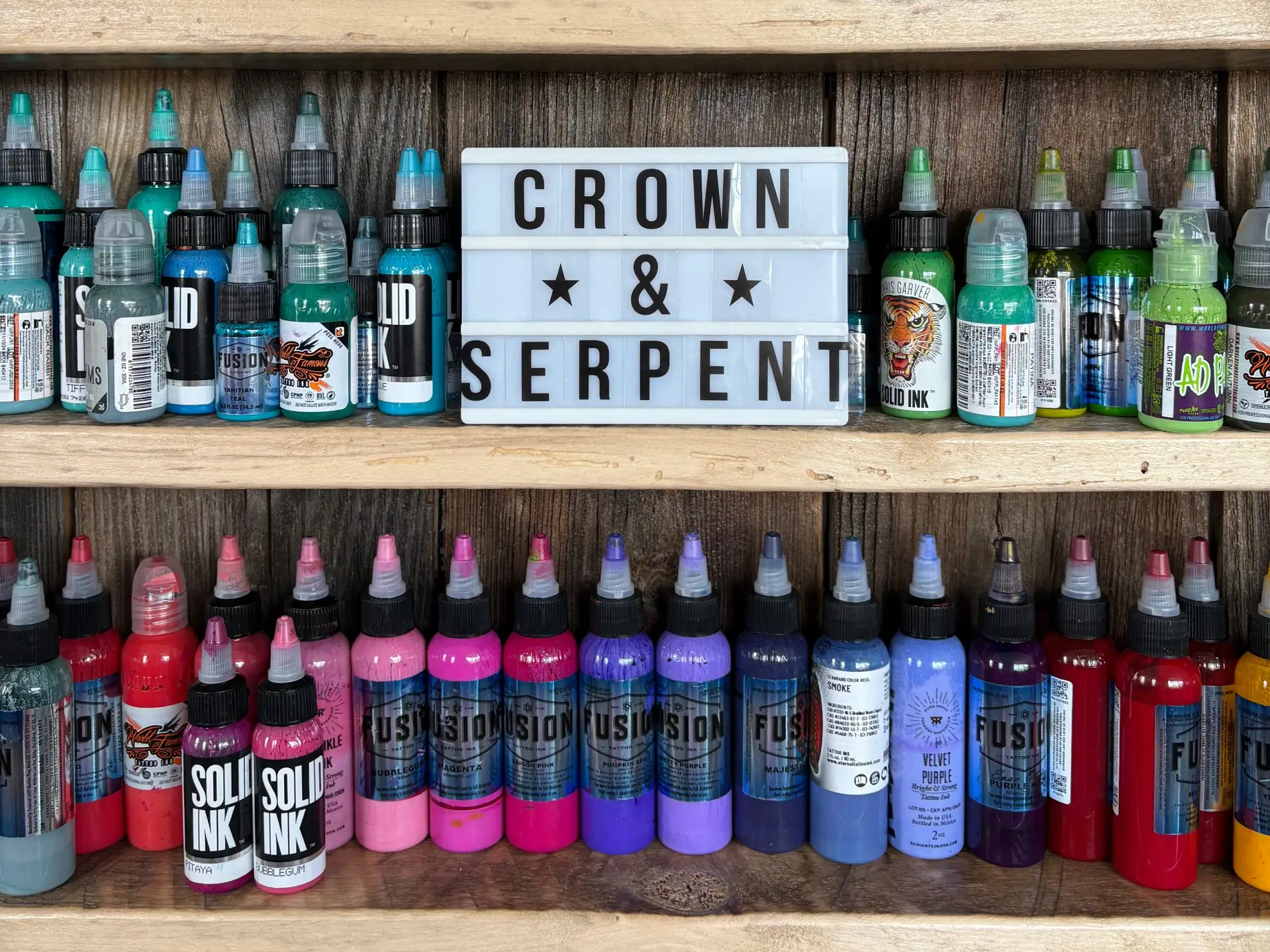 Crown & Serpent background image of a bookshelf stored with ink bottles that are sorted by color and a sign with their business name.